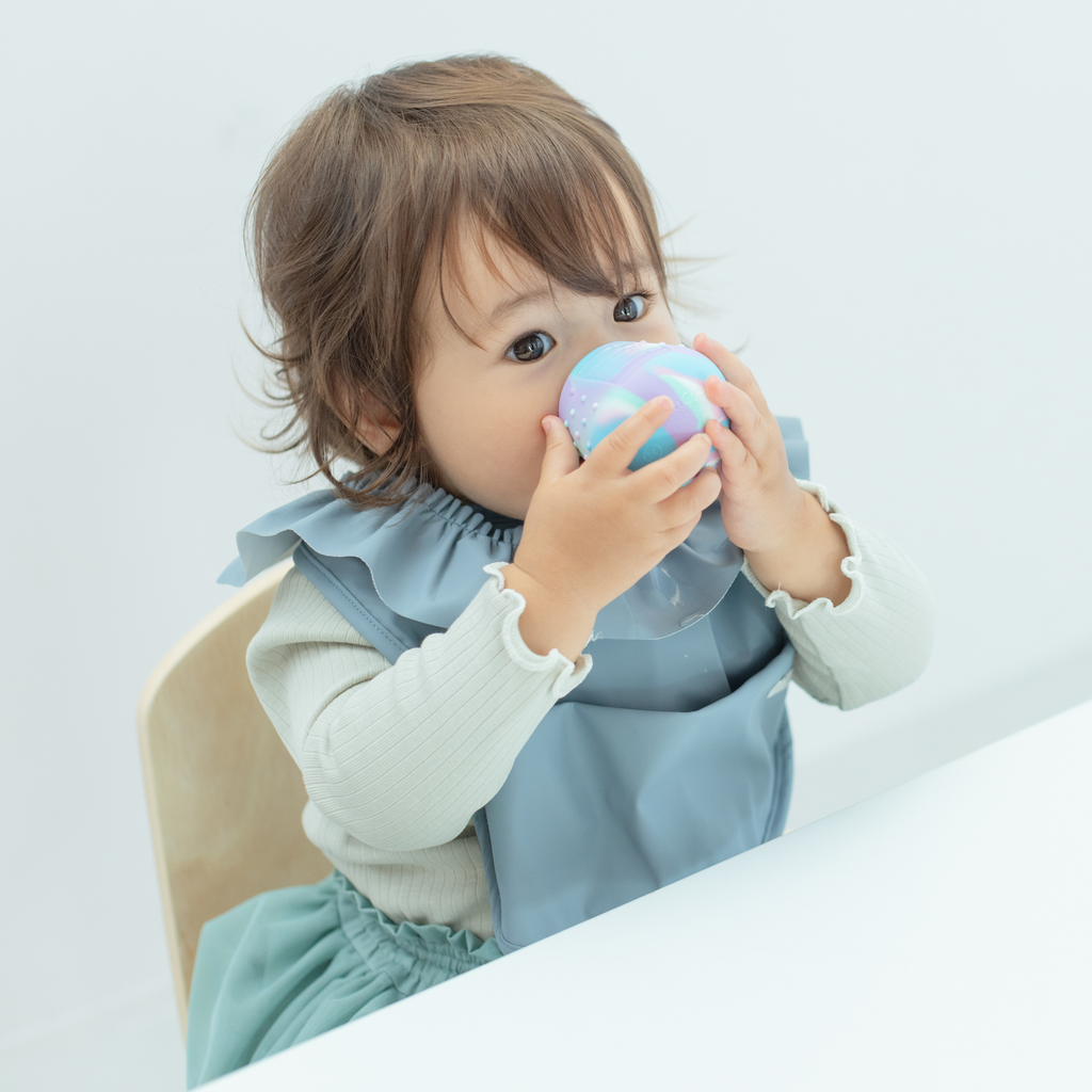 ハイチェアに座った子どもがディンキーカップを両手で持って飲み物を飲む写真